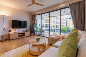 Una sala de estar moderna con una televisión de pantalla plana, una mesa de centro redonda, un sofá y un ventanal con vistas a edificios.