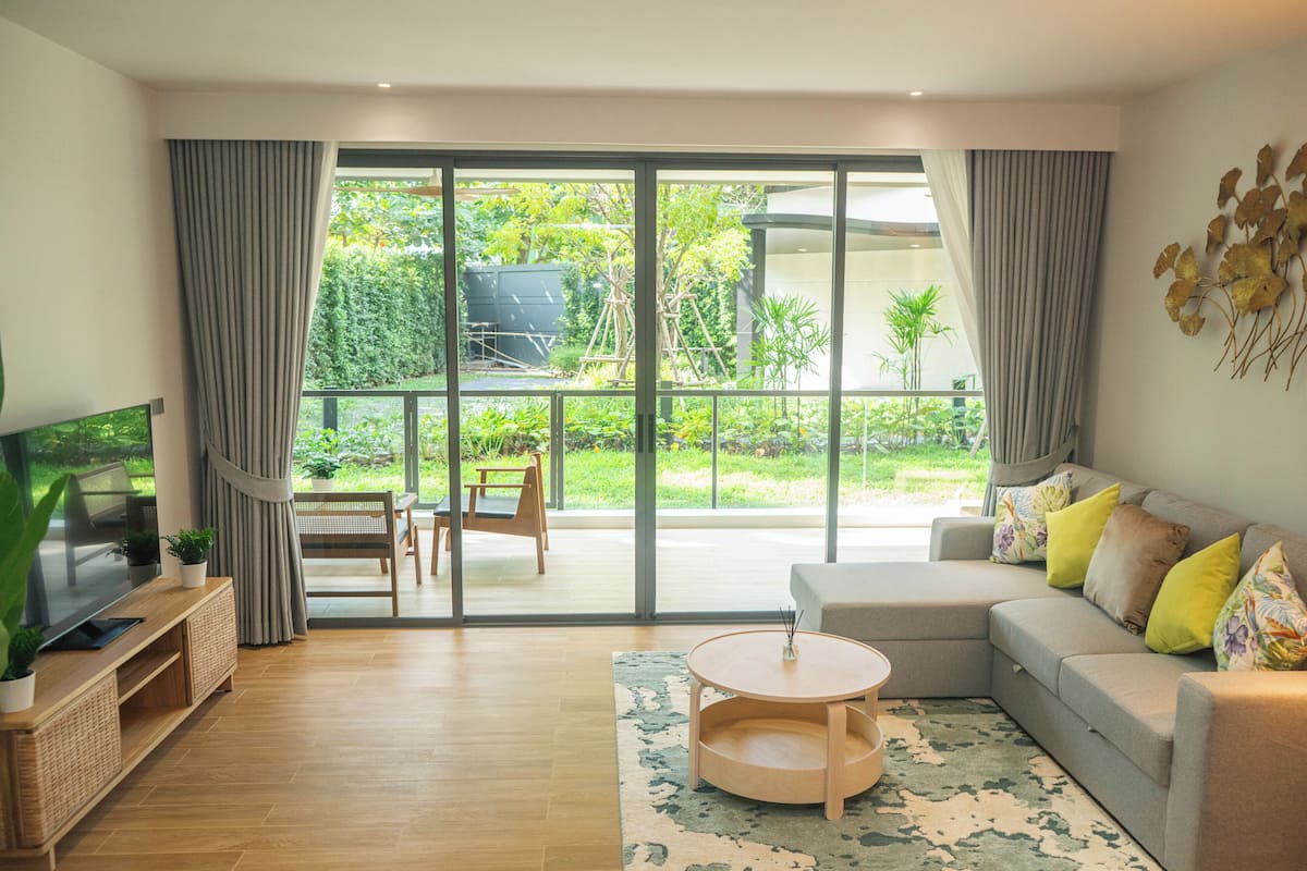 Un salon moderne comprenant un canapé, une table basse, un téléviseur et donnant sur un jardin grâce à de grandes portes coulissantes.