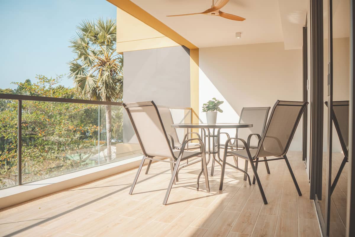 Un balcon avec une table et des chaises, un ventilateur de plafond et une vue sur des palmiers et une végétation luxuriante.