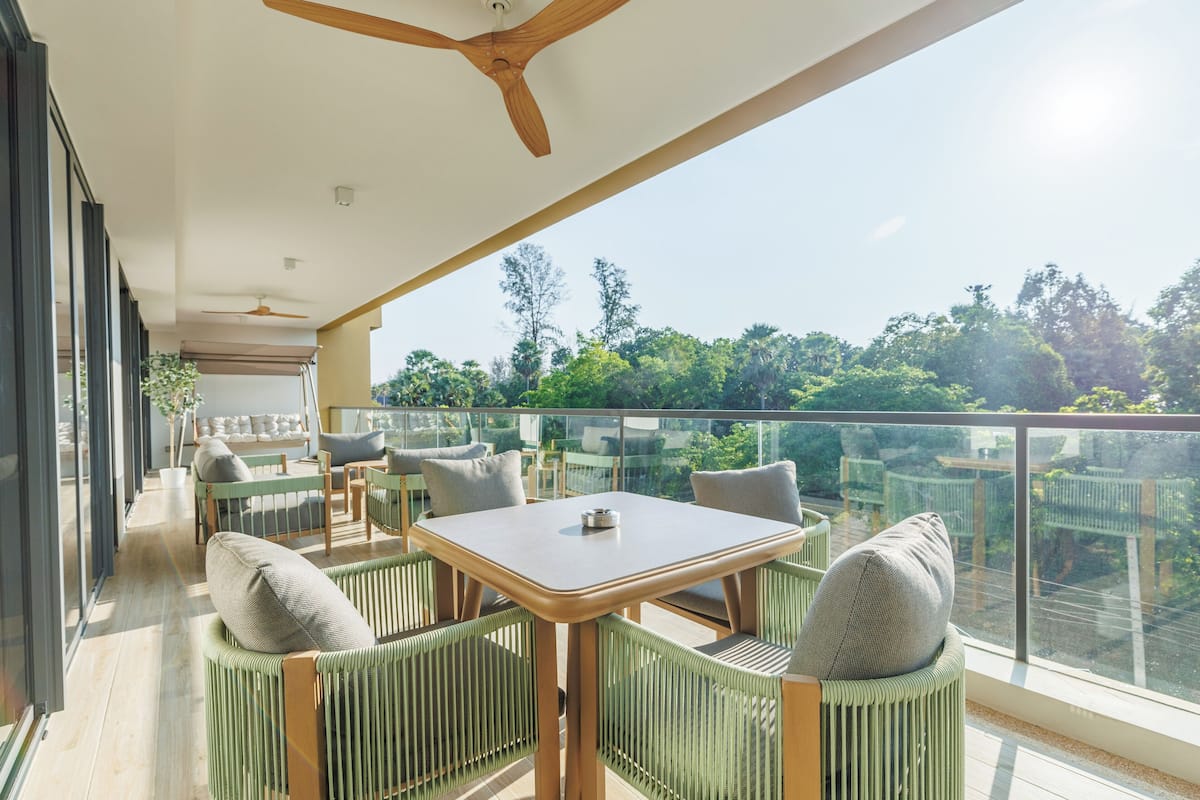 Un balcon avec une table et des chaises, un ventilateur de plafond et une vue sur les arbres.