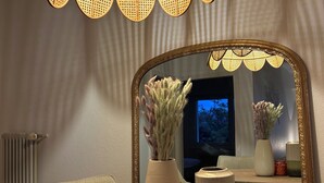 A dining area with a round wooden table, a large mirror with a decorative frame, and a hanging rattan light fixture. - L'Appart Riviera panoramic view (Blonay - Saint-Légier)