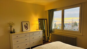 Een slaapkamer met een bed, een kapstok, een raam met uitzicht en een radiator.