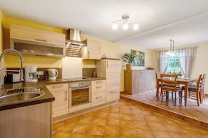 Una cocina con lavabo, estufa, armarios y una zona de comedor con sillas y mesa.
