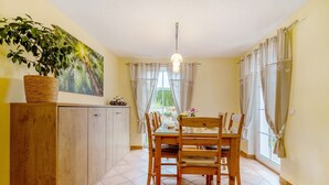 A dining area with a wooden table and chairs, a hanging light fixture, a potted plant, and a painting on the wall. - Teichmühle – Lakefront Apartment in Vogtland for Family & Pet-Friendly Holidays (Bad Brambach)