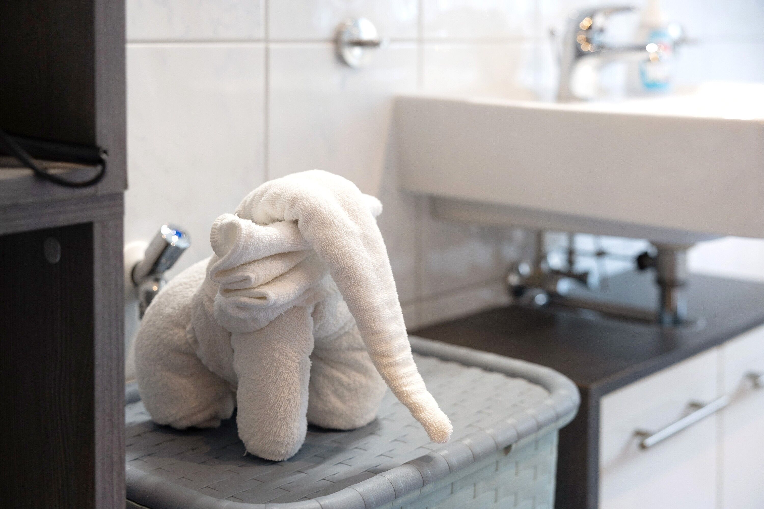 A bathroom with a white sink, a towel rack, and a plush toy elephant.