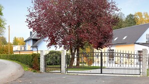 A gated residential area with a house, a tree with red leaves, and a clear sky. - Teichmühle – Lakefront Apartment in Vogtland for Family & Pet-Friendly Holidays (Bad Brambach)