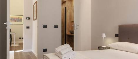 A hotel room with a bed, a nightstand with a lamp, a wooden door, and a framed picture on the wall.