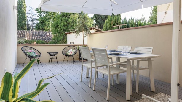 Une terrasse extérieure avec une table et des chaises blanches, un grand parasol et une vue sur un quartier résidentiel avec des arbres et des maisons.