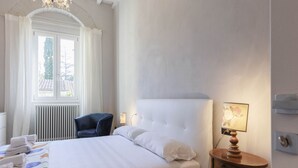 Une chambre d’hôtel avec un grand lit, une table de chevet avec une lampe, une fenêtre avec des rideaux et un radiateur.