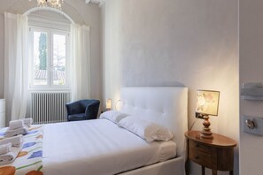A hotel room with a large bed, a bedside table with a lamp, a window with curtains, and a radiator. - Torrigiani Charming Apartment (Firenze)