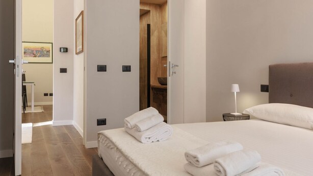 A hotel room with a bed, a nightstand with a lamp, a wooden door, and a framed picture on the wall. - Torrigiani Charming Apartment (Firenze)