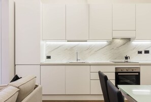 Une cuisine moderne avec des meubles blancs, un pare-feu en marbre et des appareils électroménagers intégrés.