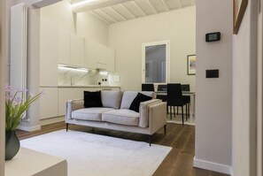 A modern living room with a white sofa, a dining area with a table and chairs, and a kitchen with white cabinets and a marble countertop. - Torrigiani Charming Apartment (Firenze)