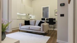 A modern living room with a white sofa, a dining area with a table and chairs, and a kitchen with white cabinets and a marble countertop. - Torrigiani Charming Apartment (Firenze)