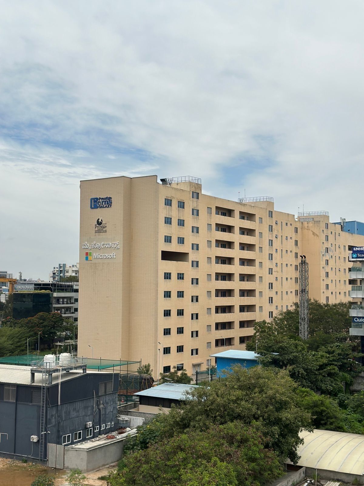 Un edificio alto de varios pisos, color beige, con el logotipo “Prestige Farns Galaxy” y la marca “Microsoft”.