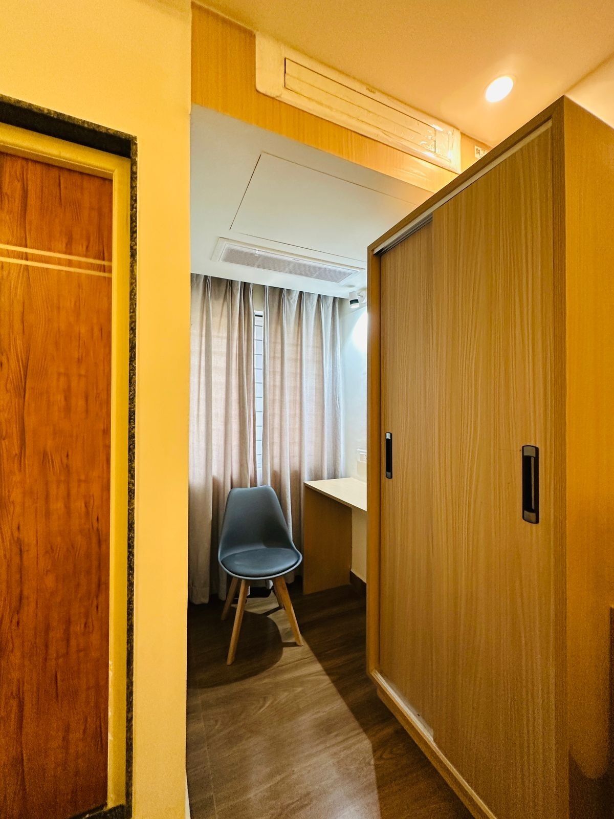 Una habitación de hotel con puerta de madera, un escritorio, una silla y una ventana con cortinas.
