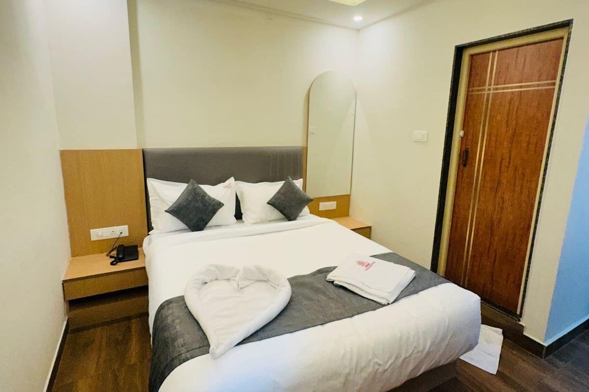 A neatly made bed with white linens, a dark wood floor, a ceiling fan, a bedside table with a phone, and a wooden door.