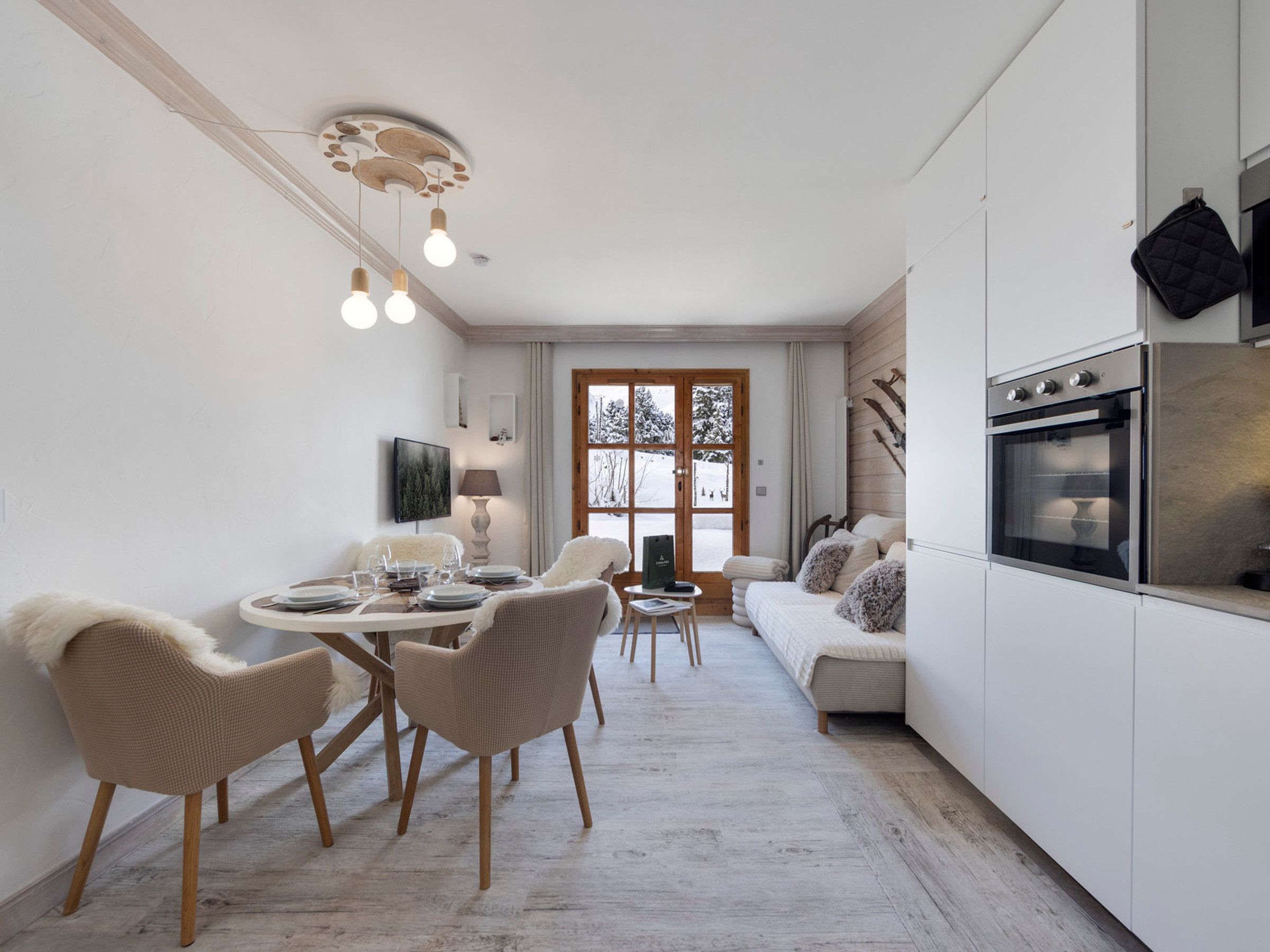 A modern kitchen with a dining area, wooden flooring, and a view through a glass door.