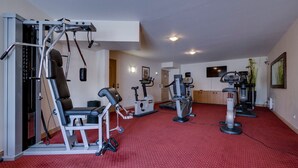 Ein Fitnessraum mit verschiedenen Trainingsgeräten, einer Bank und einem roten Teppichboden.