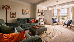 A living room with a green sofa, ottoman, and chairs, a patterned rug, and a bookshelf. - Barley Bank, a peaceful, tranquil dog-friendly retreat with a wood burning stove (Duffus)