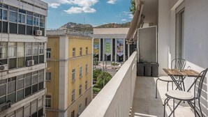 Varanda com mesa e cadeiras, vista para um horizonte urbano com edifícios e montanhas ao fundo.