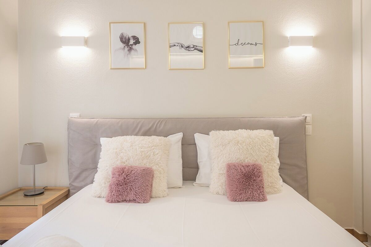 A neatly made bed with fluffy pillows, a bedside lamp, and three framed pictures on the wall.