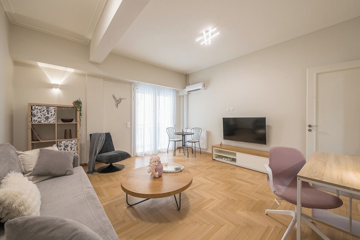 A modern living room with a sofa, coffee table, TV, and a dining area with chairs and a table.