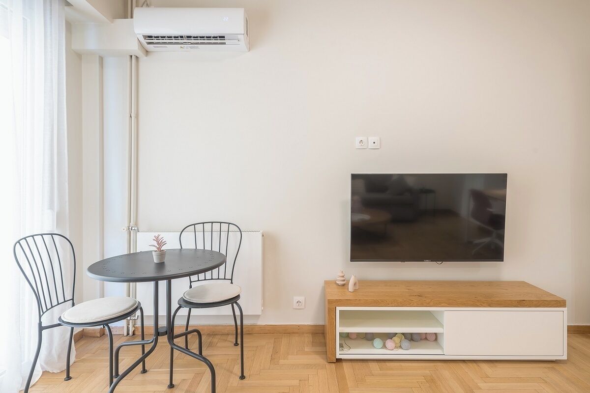 A modern living room with a round table, two chairs, a flat-screen TV, and a wooden TV stand with storage.