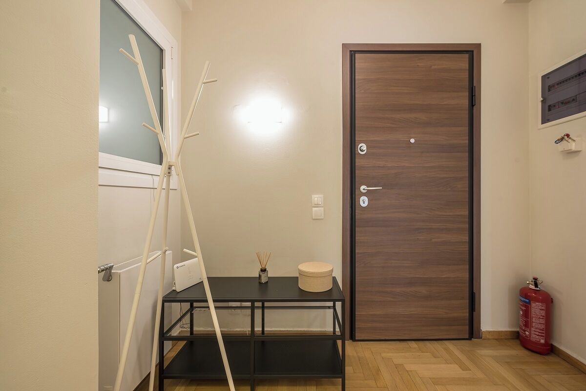 Une pièce avec une porte en bois, un radiateur, une table sur laquelle se trouvent un vase et une bougie, et un extincteur.