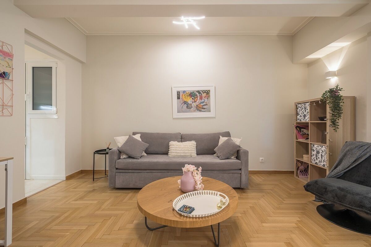 A modern living room with a grey sofa, a round coffee table with a decorative vase, and a bookshelf with various items.