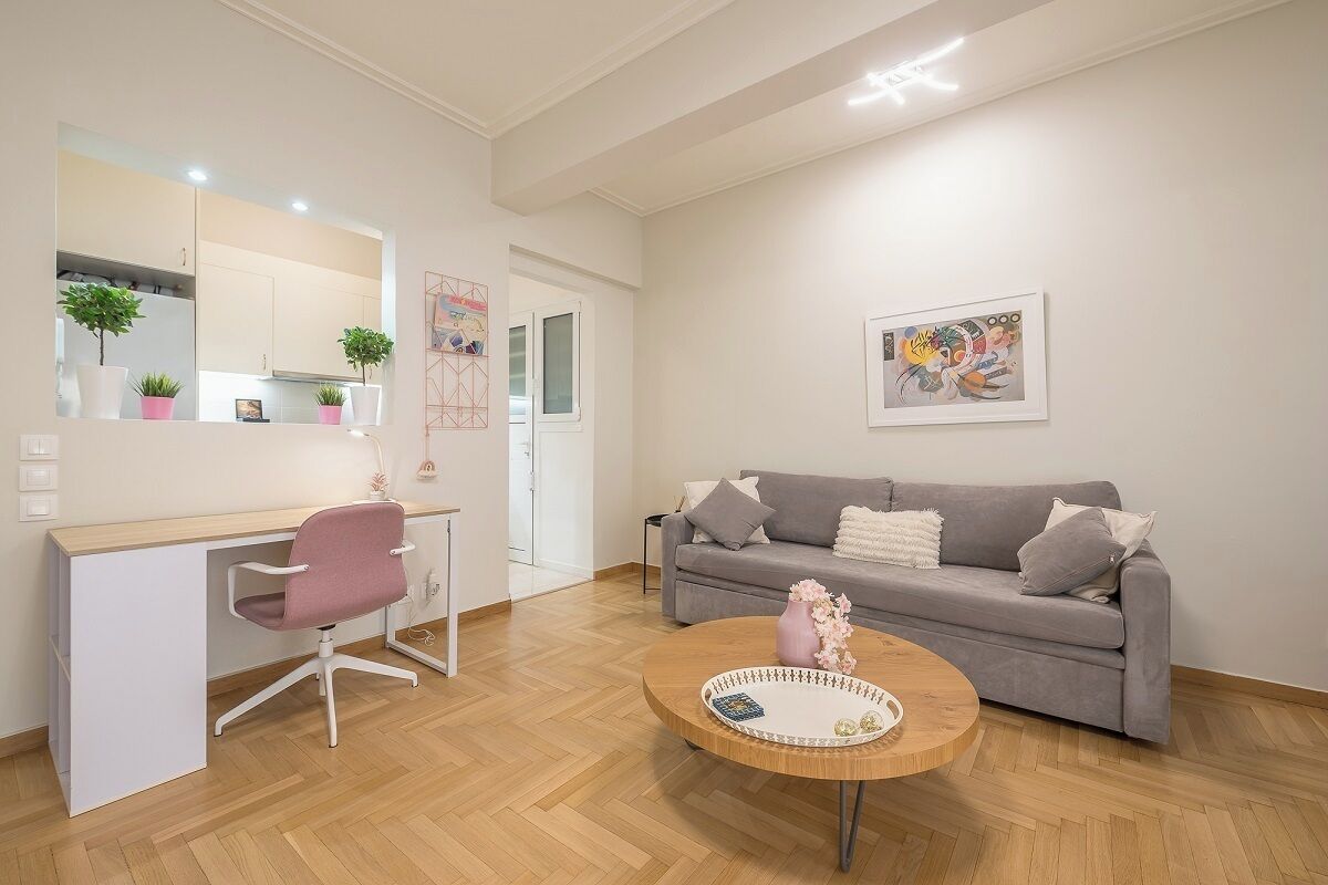 Un soggiorno moderno con un divano grigio, una poltrona da ufficio rosa, un tavolino in legno e un grande specchio che riflette la zona cucina.