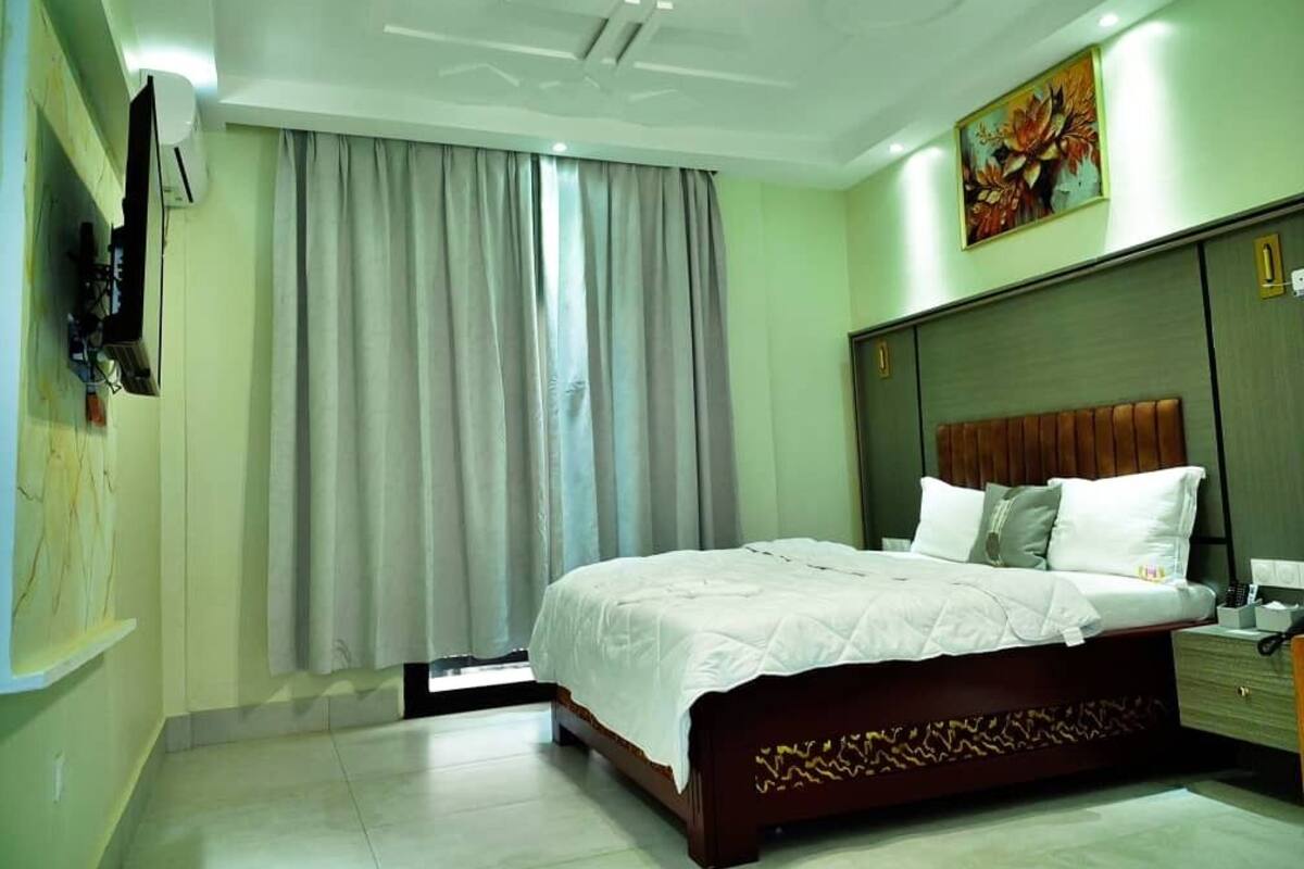 Une chambre à coucher moderne avec un grand lit, une table de chevet, un téléviseur fixé au mur et un tableau au-dessus du lit.
