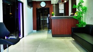 A reception area with a wooden reception desk, a clock, a black leather couch, and a plant. - Hotel Santa Bella (Douala)