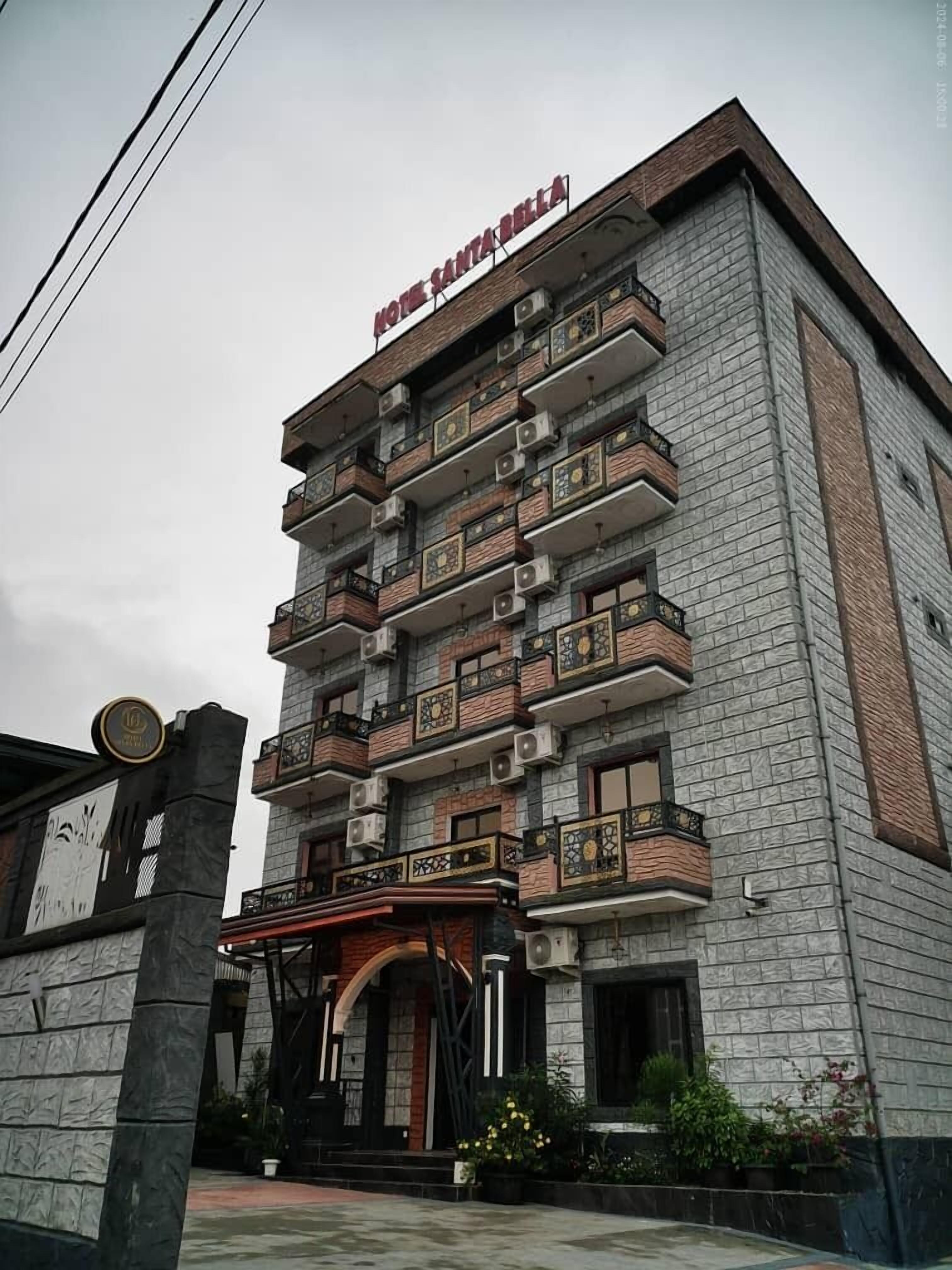 Monikerroksinen hotelli, jonka julkisivu on kivestä, ja jossa on parvekkeet jokaisessa kerroksessa. Hotellin kyltissä lukee: ”HOTEL SANTA BELLA”.