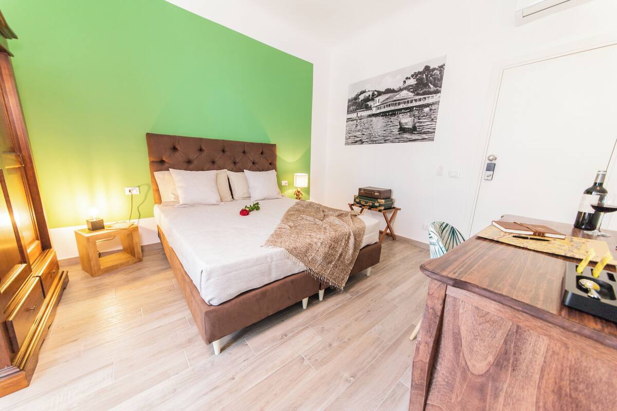 Un dormitorio con una cama grande, mesitas de noche de madera, un escritorio y una pared verde.
