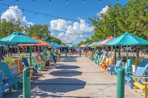 A beachside walkway with colorful Adirondack chairs and umbrellas, lined with bollards and under string lights. - Poolside Palms Villa 🌴 Resort-Style Pool | Near Beach 🏖️ (Fort Lauderdale)