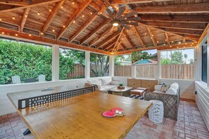 A covered patio with a wooden ceiling, a ping pong table, and seating areas.