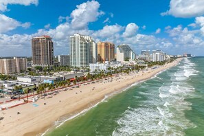 A coastal cityscape with a wide sandy beach, high-rise buildings, and a clear blue sky.