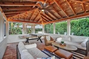 A spacious covered patio with a ceiling fan, wooden beams, and string lights.
