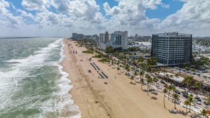 A beachside view with a hotel, palm trees, and ocean waves. - Poolside Palms Villa 🌴 Resort-Style Pool | Near Beach 🏖️ (Fort Lauderdale)