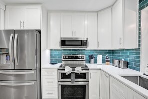 Une cuisine moderne avec des armoires blanches, des appareils en acier inoxydable et un pare-feu turquoise.