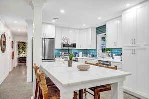 A modern kitchen with white cabinetry, a marble island, and a teal backsplash.