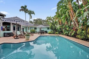 A pool area with lounge chairs and umbrellas, surrounded by lush tropical plants and palm trees.