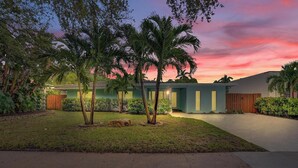 A residential property with a well-maintained lawn, palm trees, and a house with a light blue exterior. - Poolside Palms Villa 🌴 Resort-Style Pool | Near Beach 🏖️ (Fort Lauderdale)