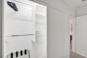 Un placard blanc, dont les portes sont ouvertes, laissant apparaître des étagères et un espace pour suspendre des vêtements.