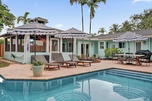 A poolside area with lounge chairs, umbrellas, and a barbecue setup. - Poolside Palms Villa 🌴 Resort-Style Pool | Near Beach 🏖️ (Fort Lauderdale)