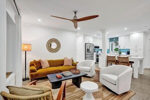 A modern living room with a sofa, armchairs, a coffee table, and a dining area with a table and chairs.