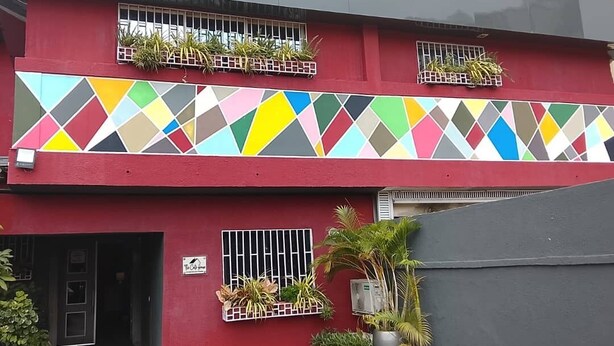 A two-story building with a red facade, a colorful geometric-patterned wall, and multiple potted plants. - The Cate House Hotel (Lagos)