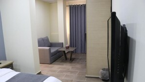 A hotel room with a bed, a small sofa, a table with a vase, and a TV mounted on the wall. - The Cate House Hotel (Lagos)