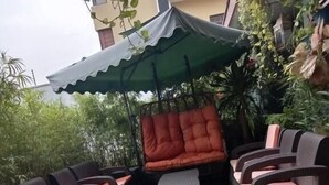 An outdoor seating area with wicker furniture and a green umbrella. - The Cate House Hotel (Lagos)